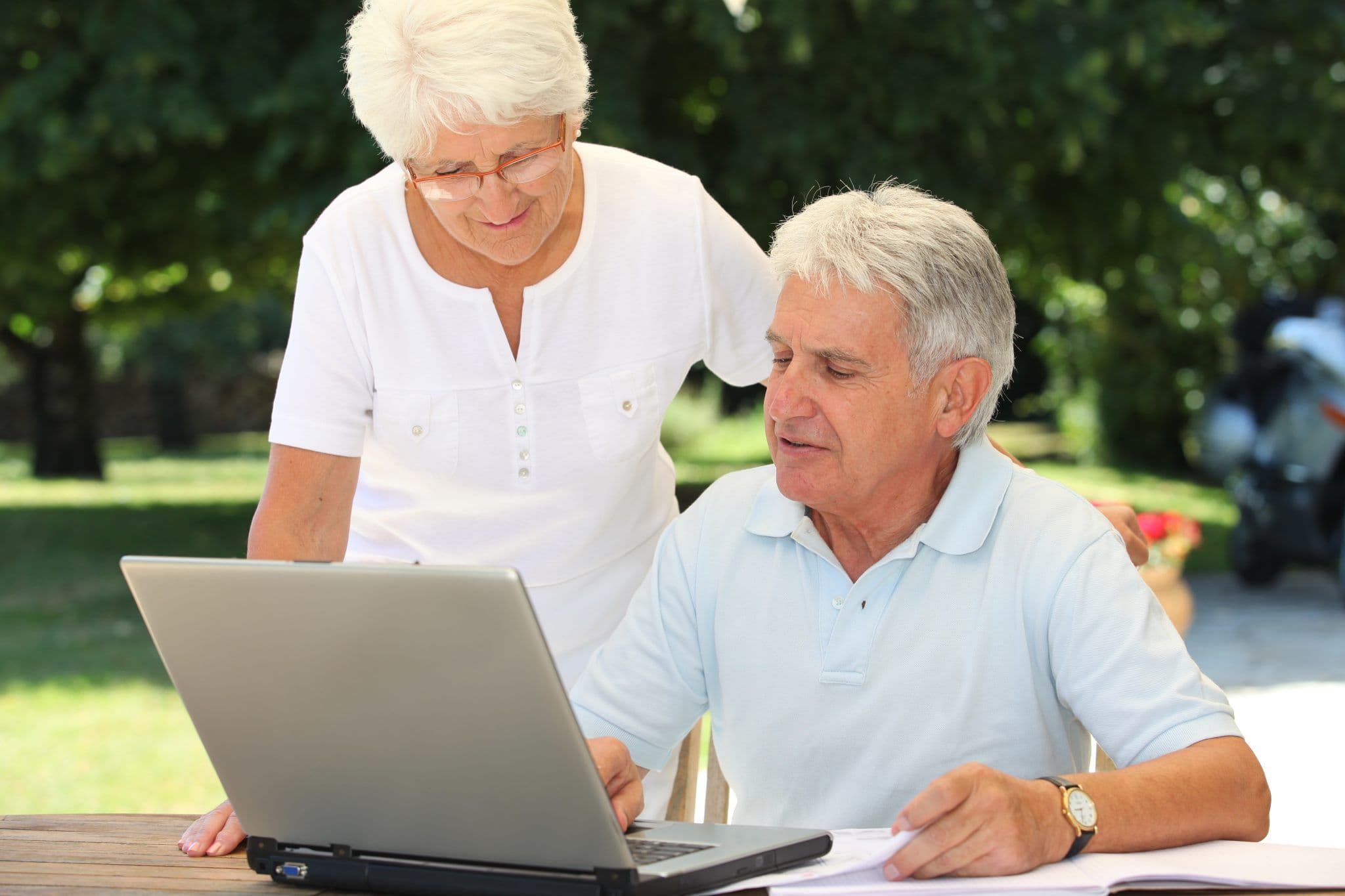 Image of an older couple using a laptop together outdoors, reviewing information on the screen with interest.